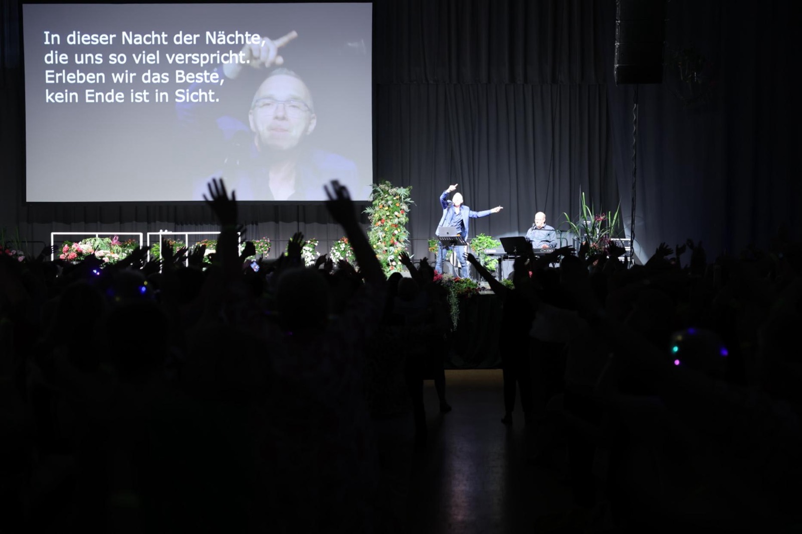 RUDELSINGEN beim Deutschen LandFrauentag 2026 - Blick ueber das Publikum mit erhobenen Armen auf Buehne und Songtext-Leinwand